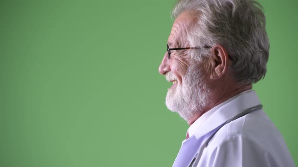 Handsome Senior Bearded Man Doctor Against Green Background