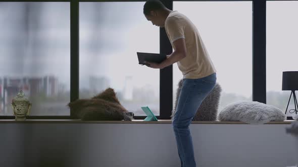 Wide Shot of African American Man Walking in Slow Motion to Window in Home Office Sitting Down and