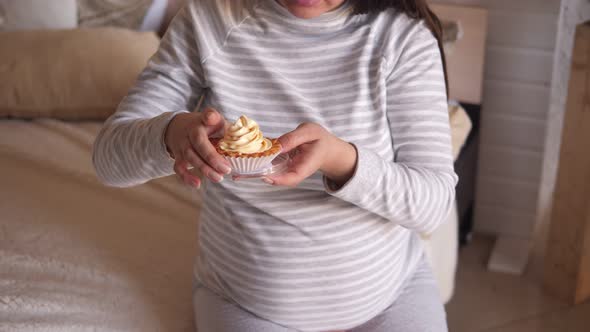 Closeup of a Pregnant Woman Holding a Sweet Cake While Sitting on the Bed