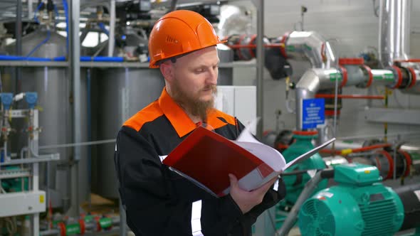 A Male Industrial Equipment Operator Stands in the Oil and Gas Pumping Shop of a Pumping Station