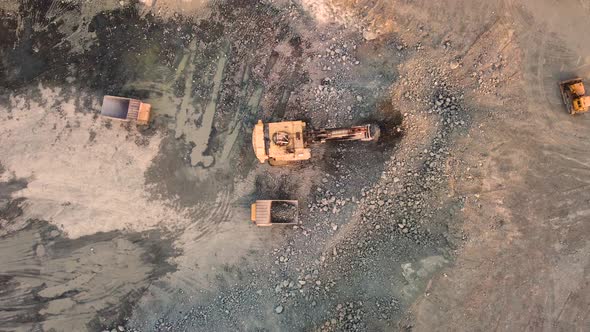 Aerial top down view of an excavator loading crushed stone into a dump truck