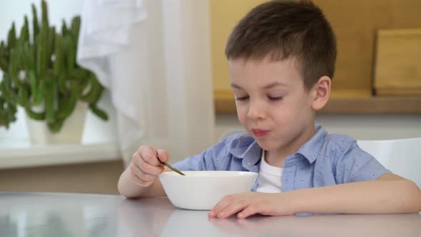 Small Hungry Boy Eating Tasting Sweet Corn Flakes with Milk at Morning