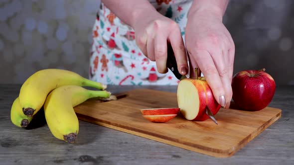 A slim young woman in a kitchen cutting up a red apple on a chopping board