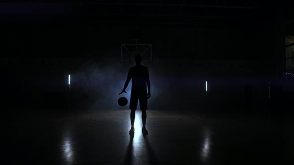 Basketball Player Knocks the Ball in the Light of the Lamps Shining Behind Stands in the Duma and