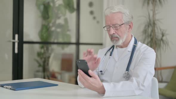 Attractive Senior Old Doctor Using Smartphone in Clinic