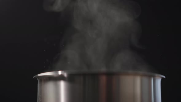 Slow Motion Closeup of Steam Rising From Steel Pot Over Black Background