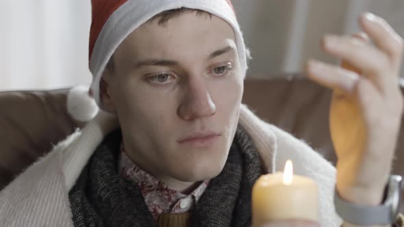 Headshot of Lonely Young Caucasian Man in New Year Hat Blowing Out Candle