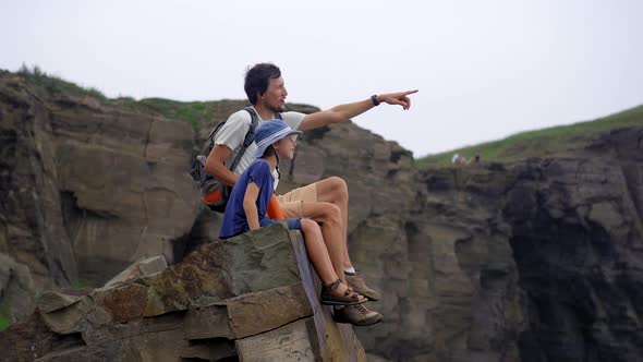 A Young Man and His Son are on a Hike Among Rocks Near the Sea