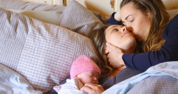 Lesbian couple romancing while relaxing with their baby boy in bedroom 4k