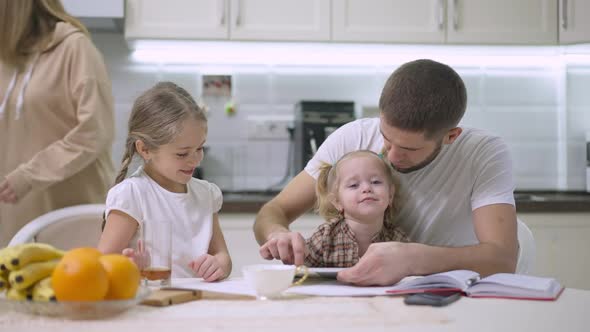 Cute Daughters Enjoying Morning with Father in Kitchen As Mother Passing at Background in Slow