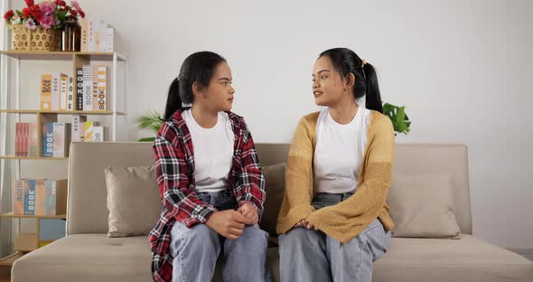 Sad young twin girls sit back to each other after a quarrel with her twin sister.