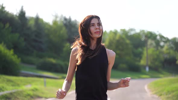 Athletic Woman Listening Music on Earphones While Running at Road in the Morning