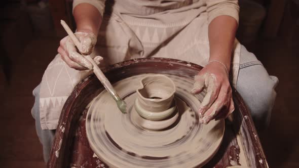 Young Woman Potter Shaping Wet Clay Using a Brush