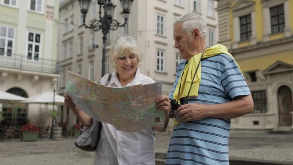 Senior Male and Female Tourists Walking with a Map in Hands Looking for Route