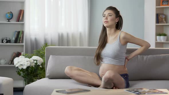 Expecting Female Sitting on Couch and Stretching Back, Touching Her Stomach