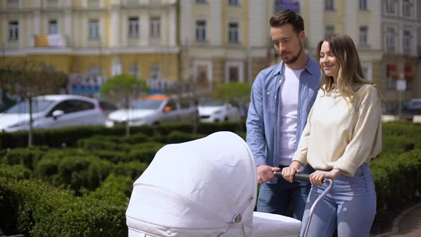 Smiling Young Parents Walking in City Garden Pushing Newborn Pram, Parenting