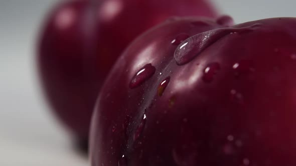 A drop of pure water drips and splashes onto the textured rind of a ripe red plum