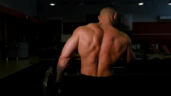 Powerlifter Shakes His Biceps with Dumbbells, Back View Close-up