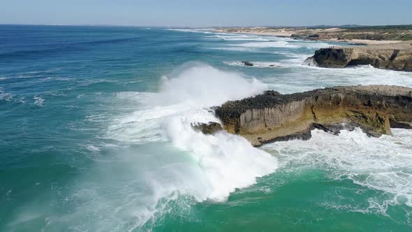 Coast of Portugal. Turquoise and Foamy Ocean Waves Hitting Rocks. Rainbow Is Seen Just Above Water