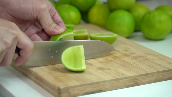 Hand Slicing fresh Lime With Knife On Wooden Board In Kitchen