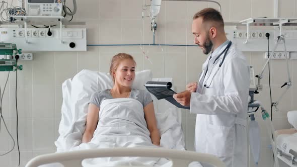 Male Doctor Talking to Female Patient in Hospital Bed