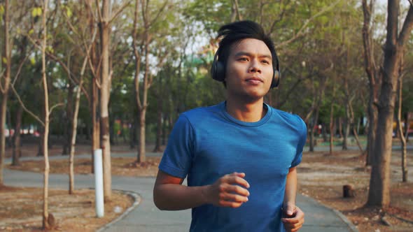 Slow-motion Asian athletic man wearing headphone listening to music during running in the park.