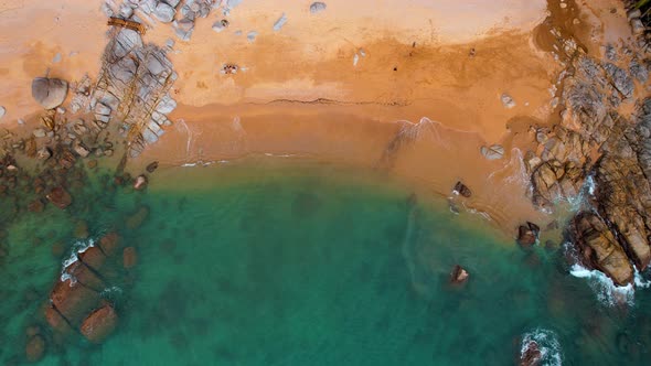 Aerial Top Down View of Sea Waves Breaking and Foaming on a Sandy Tropical Beach with Large Stone