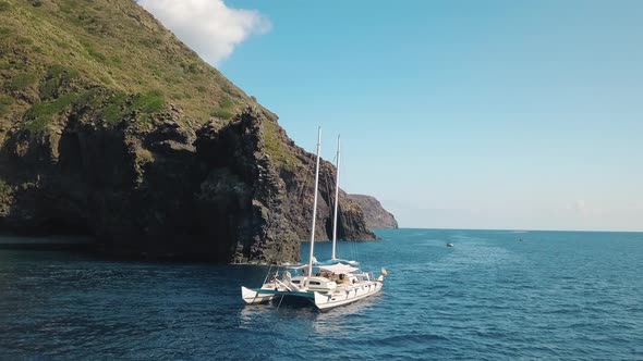 Aerial View on White Catamaran with Flags of Ukraine and Europe Union Against Rock of Lipari Island