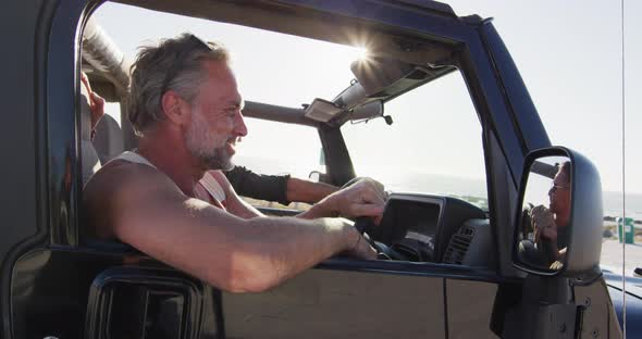 Happy caucasian gay male couple in car admiring the view and pointing on sunny day at the beach