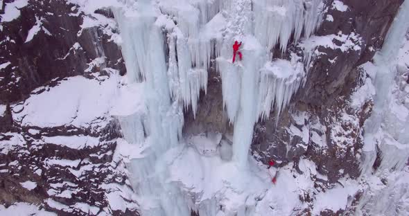 Aerial drone view of a man ice climbing on a frozen waterfall in the mountains