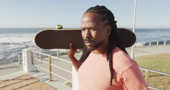 Video of african american man holding skateboard by sea