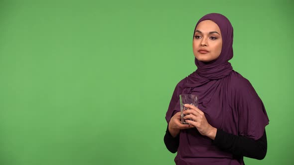 A Young Beautiful Muslim Woman Drinks Water From a Glass Then Smiles at the Camera  Green Screen