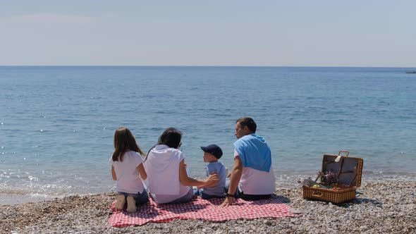 Family with boy and girl sitting with back forward at beach on sunny summer day.