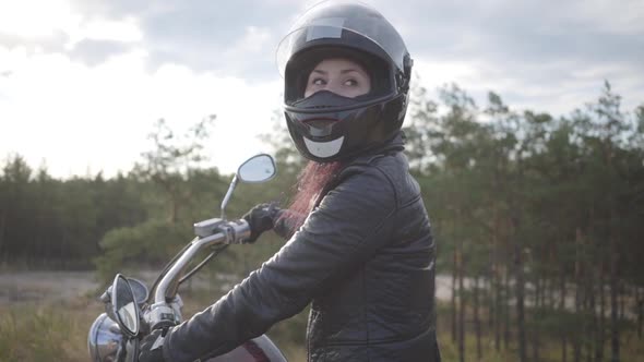 Confident Girl Wearing Black Helmet Sitting on the Motorcycle Looking Back on the Road