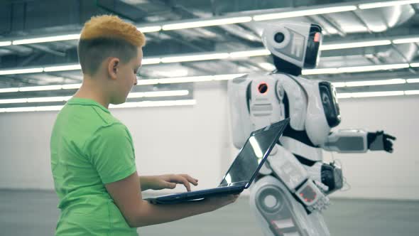 Boy Controls Droid, Using a Laptop. Futuristic Humanoid Robot