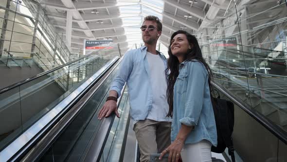 Smiling Man and Woman Going Up the Escalator While Looking at the Train Station