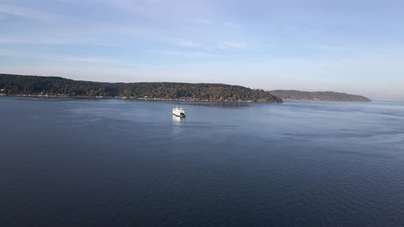 Fall colors dot the shoreline as a vessel ferry crosses calm blue waters, aerial