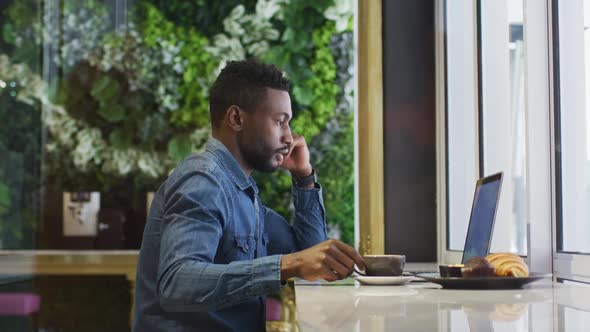 African american businessman using laptop drinking coffee in cafe