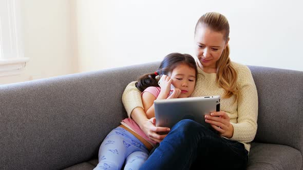 Mother and daughter using digital tablet in living room