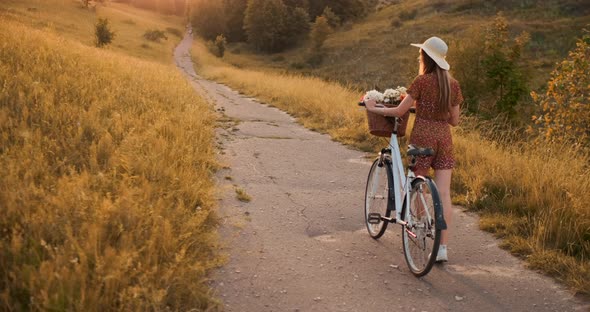 A Girl in a Hat with a Bicycle Turns Around and Looks at the Camera Smiling