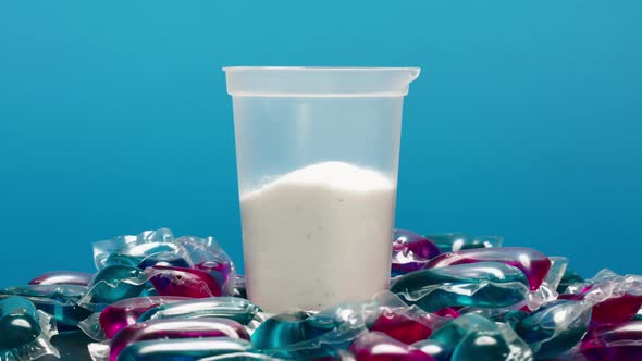 Washing Gel Pods and Plastic Glass with Detergent Powder on Blue Background Capsules with Detergent