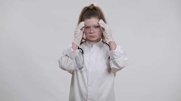 Front View Portrait of Charming Confident Little Doctor Putting on Transparent Eyeglasses Looking at