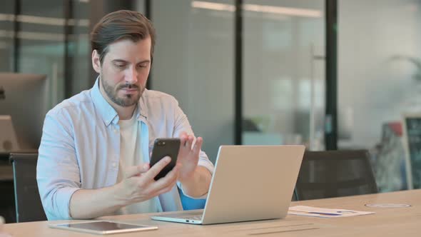 Mature Adult Man with Laptop Using Smartphone in Office