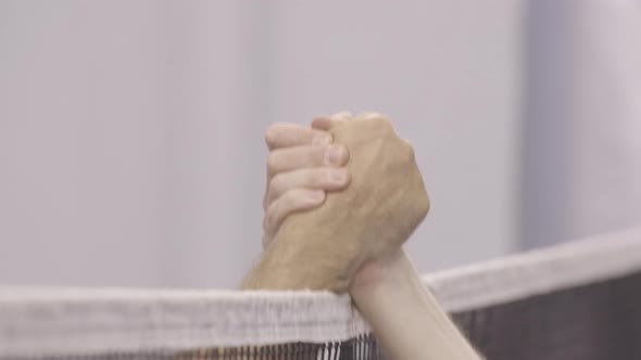 Close-up of Two Male Caucasian Hands Shaking Over Badminton or Tennis Net in Gym. Unrecognizable