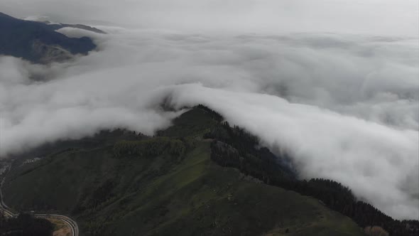 Aerial above white clouds covered mountains in valley during rainy weather