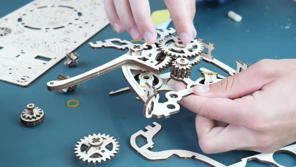 Man assembling mechanical wooden puzzle toy on table.