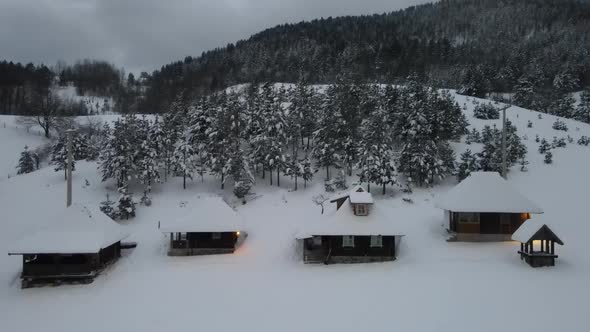 Mountain wooden houses covered with snow with trees and dark clouds in back. Aerial shot.