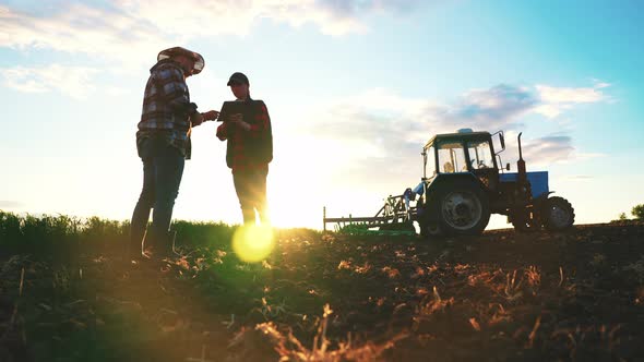 Man Farmer and Female Agronomist on Agricultural Field in Spring Morning Tractor on Farmland Sowing