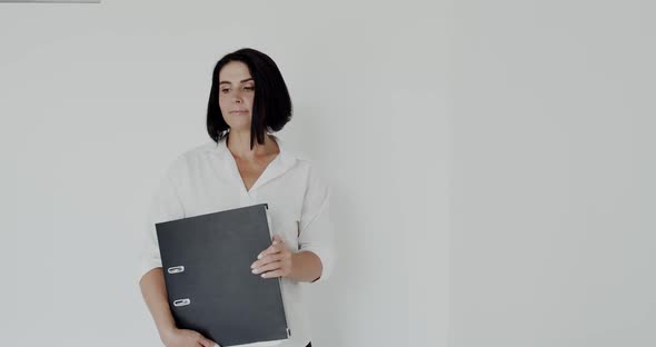 Confident Teacher with Folder in Hands Poses with Smile on Face on Background