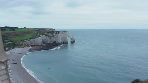 Small Church on Hill, Aerial Forward Revealing Etretat Cliffs in France with Overcast Sky